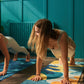 Two women practicing yoga on colorful mats in a room with blue walls and plants.