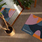 Colorful abstract-patterned yoga mat on a wooden floor with plants and furniture.