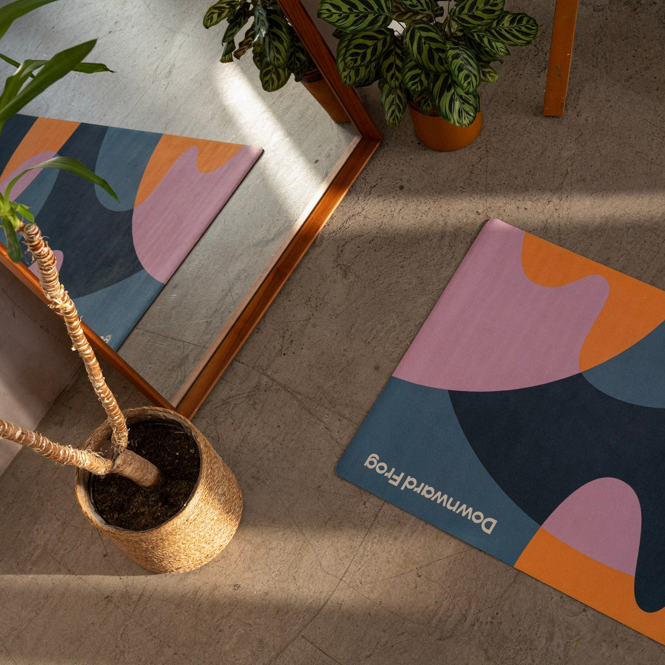 Colorful abstract-patterned yoga mat on a wooden floor with plants and furniture.