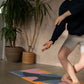 Person practicing yoga on a colorful mat with plants in the background