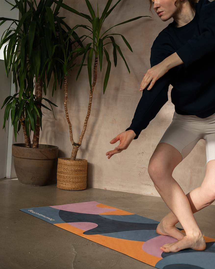 Person practicing yoga on a colorful mat with plants in the background